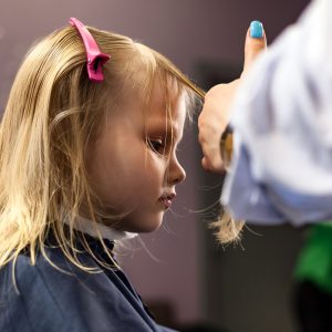 Barber female make fashionable hairstyle for little blond girl child in barbershop. Hairdresser makes hairdo for baby in barber shop. Hairstyle, hair salon, beauty concept. Copy advertising text space