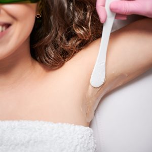 Close up of cosmetologist applying gel on female underarm before laser epilation procedure. Smiling young woman receiving laser hair removal treatment in beauty salon.