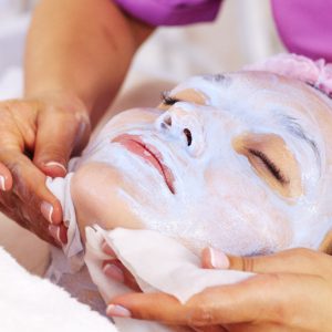 Cosmetologist removing  a mask scrub from female face. Woman in a spa salon on cosmetic procedures for facial care.