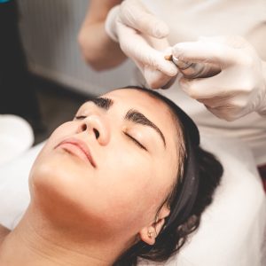 Cosmetologist smears face of patient with nourishing cream