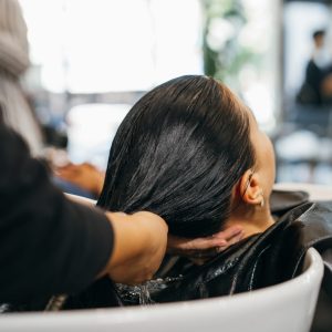 Young Caucasian woman at the hairdresser pampering herself by getting her hair washed and rinsed with eyes closed with head in sink for hairwash