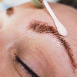 Close up of an unrecognizable beautician doing eyebrow lamination procedure to a beautiful female model.