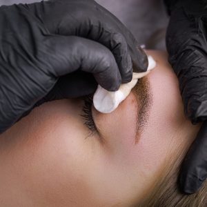 Remove excess pigment from the eyebrows with a cotton sponge. PMU Procedure, Permanent Eyebrow Makeup.